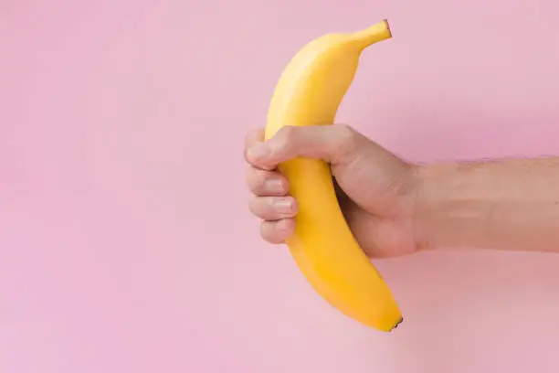 Male hand holding a banana isolated on pink background.