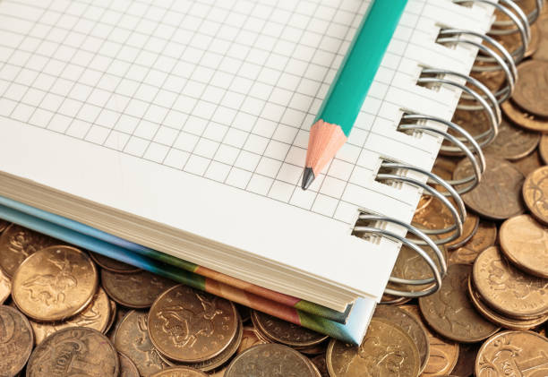 istock Notepad and pencil on a pile of coins 871558858