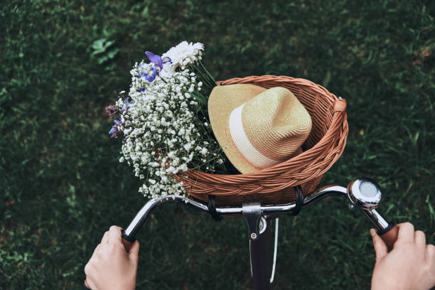 Spring time! Close-up of woman riding on a bicycle with flowers and a hat in the basket bicycle basket stock pictures, royalty-free photos & images