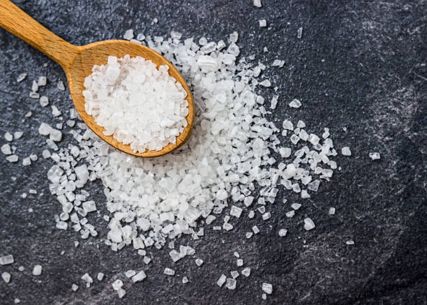 istock Sea salt in a wooden spoon on a black background. 871582162