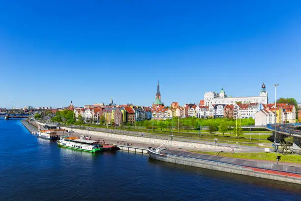 Large river barge and sightseeing ships moored to the embankment in Odra River, Old Town of Szczecin in background