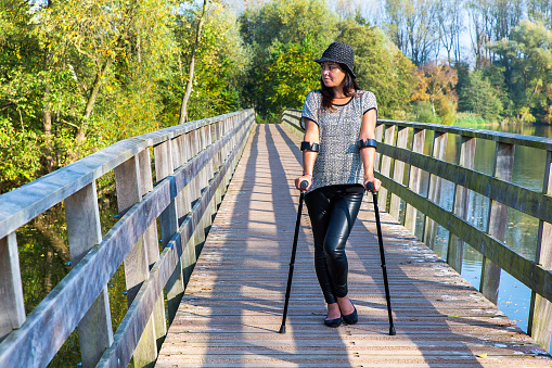 Woman with crutches standing on bridge