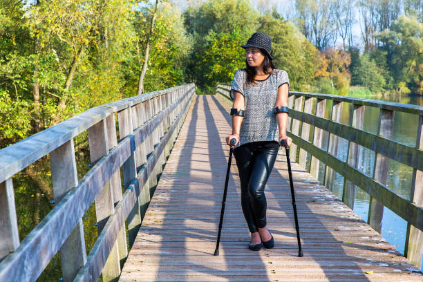 Woman with crutches standing on bridge Young woman walking with crutches on wooden bridge over water. This young woman with long hair is dressed in black. Because the person is injured, she now walks with crutches as a tool to lean on. In this way she still can enjoy the beautiful landscape in dutch nature. disabled person hiking outdoors stock pictures, royalty-free photos & images