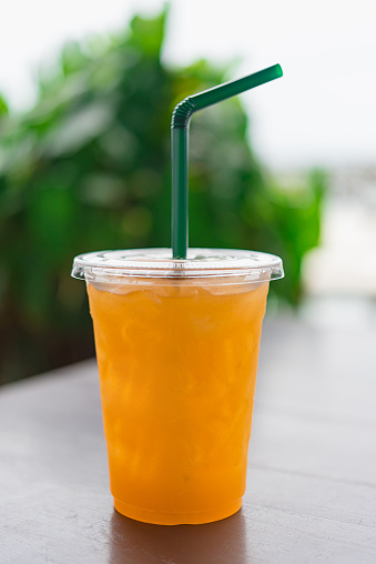 Orange juice  in a plastic glass placed on a wooden table.Fresh orange juice with straw and slice in take away cup.