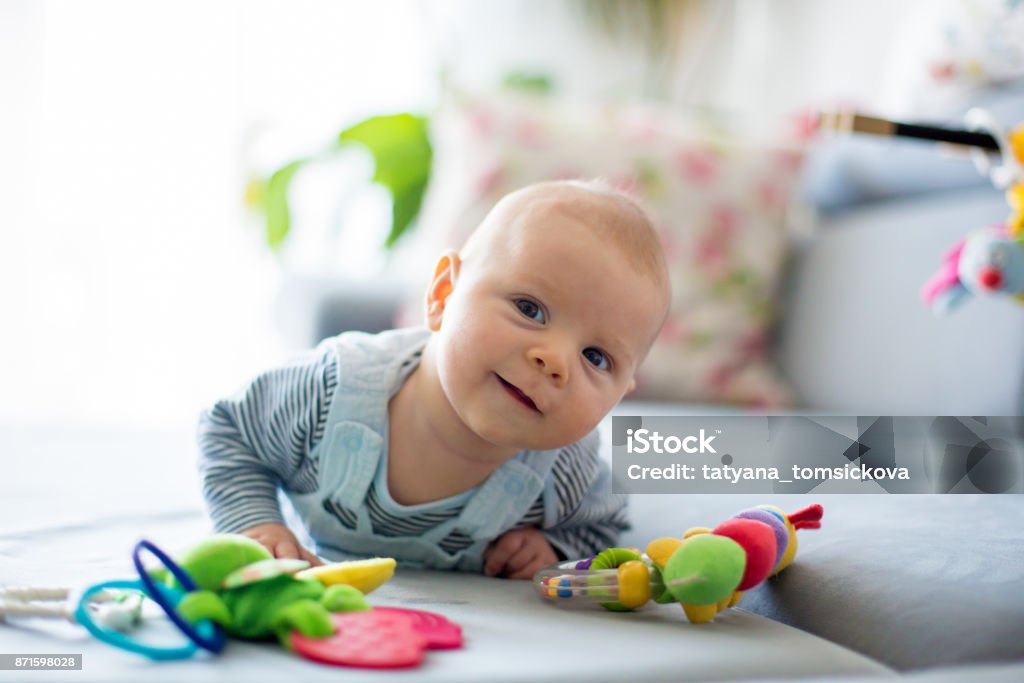 Cute baby boy, playing with toys in a sunny living room Cute baby boy, playing with toys in a sunny living room, lying down on the sofa Baby - Human Age Stock Photo