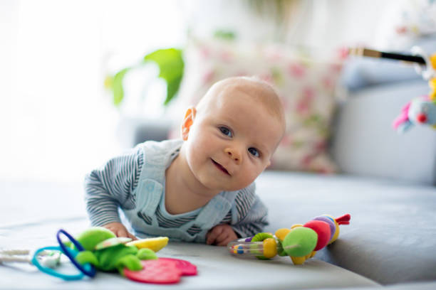 Cute baby boy, playing with toys in a sunny living room Cute baby boy, playing with toys in a sunny living room, lying down on the sofa baby toys stock pictures, royalty-free photos & images