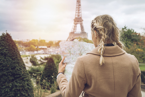 Beautiful blond woman in Paris looking at street map for directions. Tourist looking for sightseeing and location inn the city. Shot at Trocadero, view on the Eiffel Tower, France.