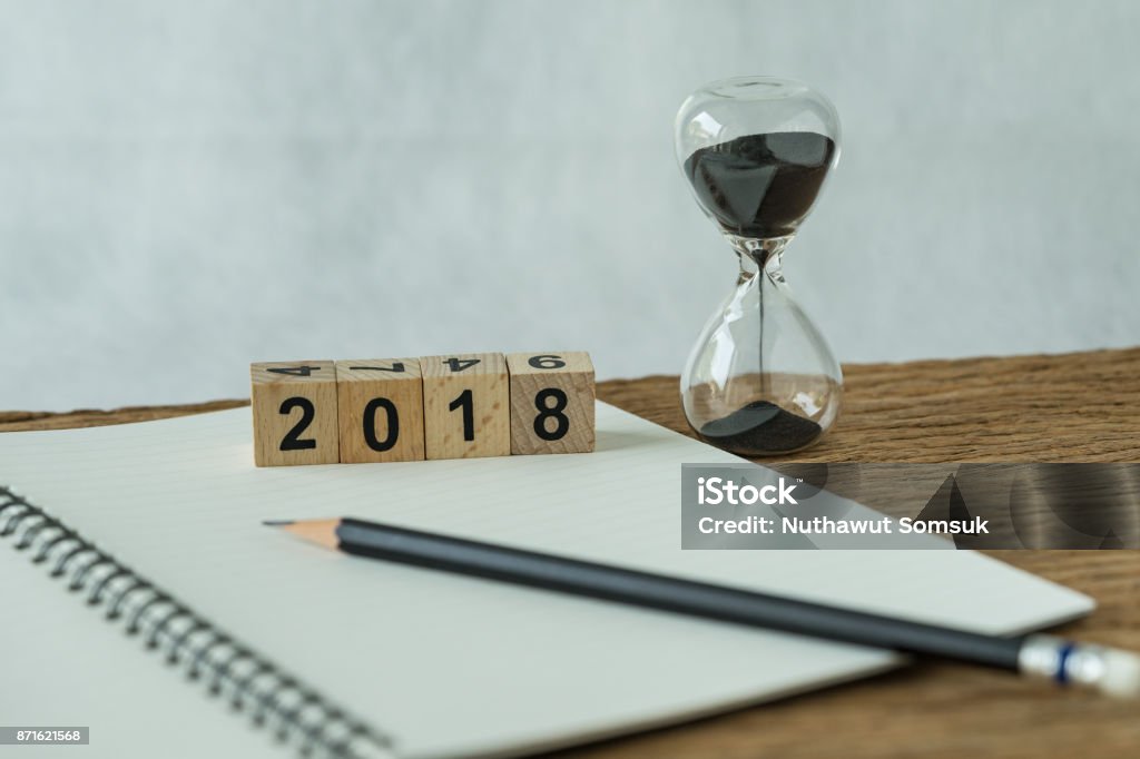 objectifs de la nouvelle année 2018, concept cible ou liste de contrôle comme pavé numérique de 2018 cube en bois avec sablier et livre blanc note au crayon sur la table en bois - Photo de 2015 libre de droits