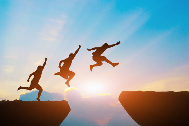 istock Men jump cliff sun light over silhouette 871625406