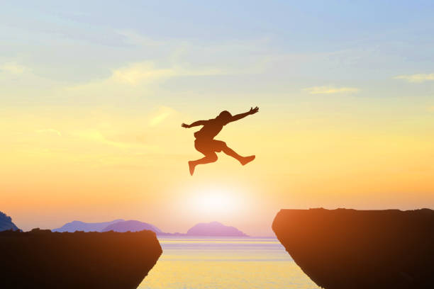 istock Men jump cliff sun light over silhouette 871625410