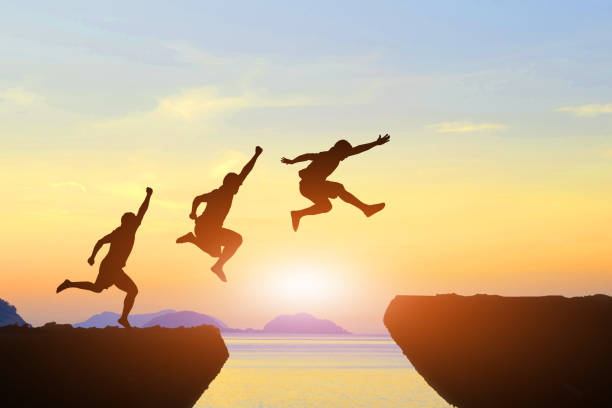 istock Men jump cliff sun light over silhouette 871625430