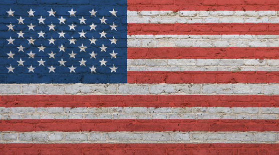 Old grunge vintage American US national flag graffiti over background of white brick wall