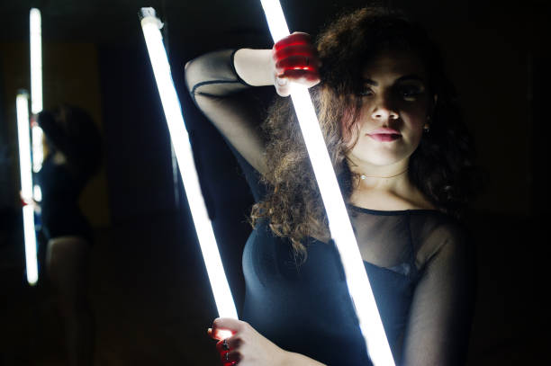 istock Curly brunette plus size model with two long led lamp at dance room with mirror. 871634958