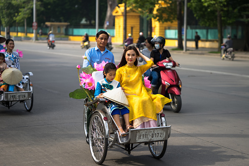 Hanoi: Vietnamese girl wears traditional long dress Ao Dai going by Cyclo (pedicab) on Hanoi street