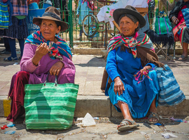 Two indigenous women of the Tarabuco indigenous minority chatting and talking, sitting on the sidewalk, on the sunday market. Photographed in Tarabuco, Bolivia, South America.