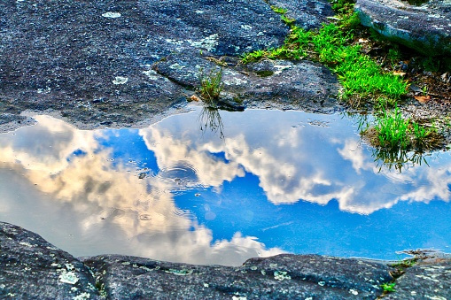 Clouds from sky reflecting off puddle of water