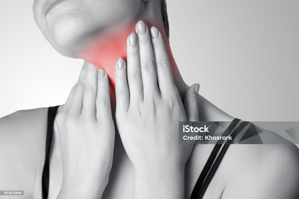 Closeup view of a young woman with pain on neck or thyroid gland on gray background. Closeup view of a young woman with pain on neck or thyroid gland on gray background. Black and white photo with red dot. Cancer - Illness Stock Photo