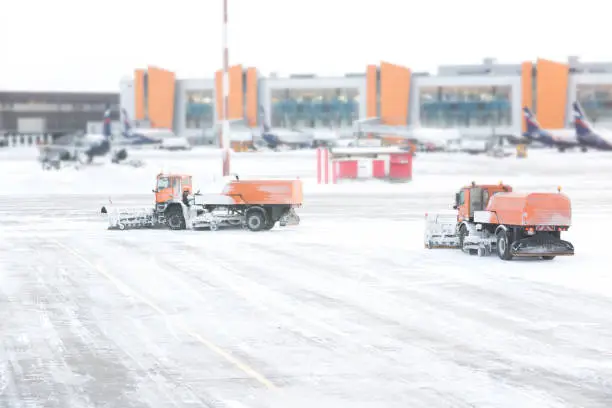 Snowplow removing snow from runways and roads in airport during snow storm, view through windowSnowplow removing snow from runways and roads in airport during snow storm, view through window
