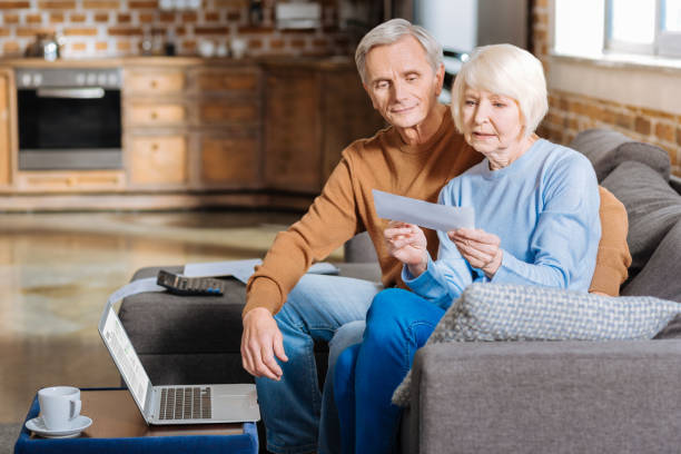 Serious elderly woman checking financial documents Payment notification. Serious unhappy elderly woman sitting together with her husband and looking at the document while holding it retirement social security stock pictures, royalty-free photos & images