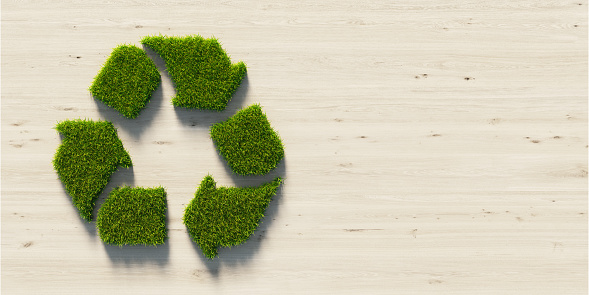 Recycling symbol made of green grass on wood background. Horizontal composition with copy space. Green energy concept.