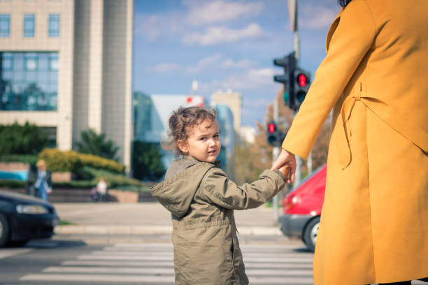 istock Small girl holding mother's hand while standing on zebra crossing. 871717498