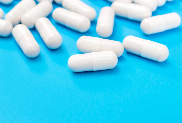 Lot of white capsules on a blue background. Medical background. stock photo