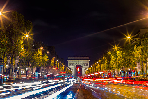 Illuminated Arc de Triomphe and the avenue Champs-Elysees in Paris. Famous touristic places and transportation concept. Night urban landscape with street traffic and city lights. Long exposure. Toned.