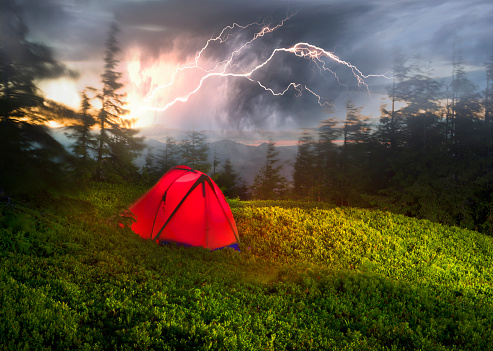 tent is illuminated at the top of the mountain, the waves of the misty sea float in the valley against the backdrop of high peaks covered in forests. Dangerous electricity in a hike