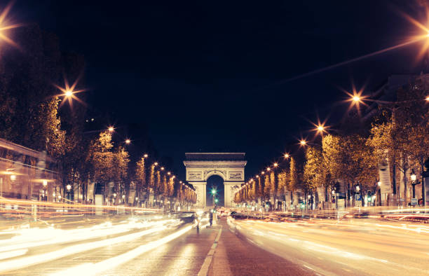 Illuminated Arc de Triomphe and the avenue Champs-Elysees in Paris. Famous touristic places and transportation concept. Night urban landscape with street traffic and city lights. Long exposure. Toned stock photo