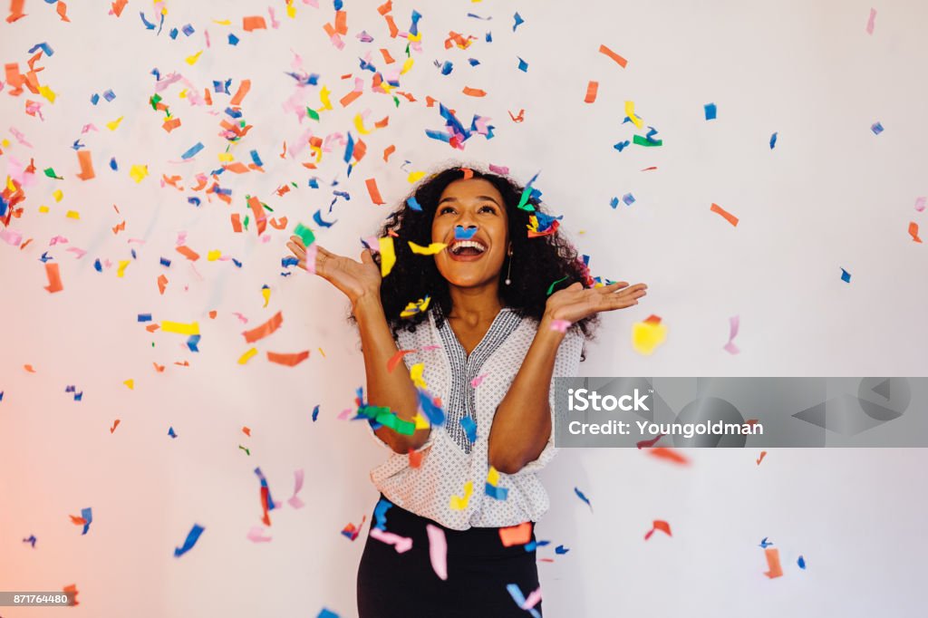 Giovane donna in piedi al chiuso sotto coriandoli colorati - Foto stock royalty-free di Festeggiamento