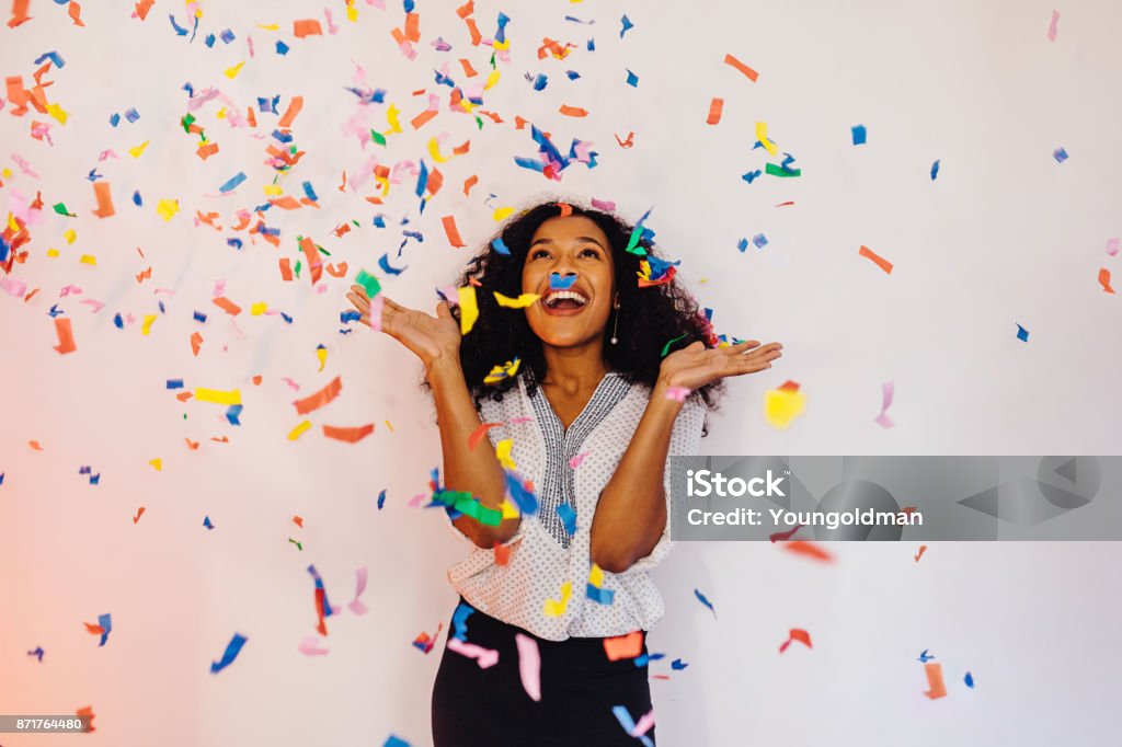 Young woman standing indoors under colorful confetti Celebration Stock Photo