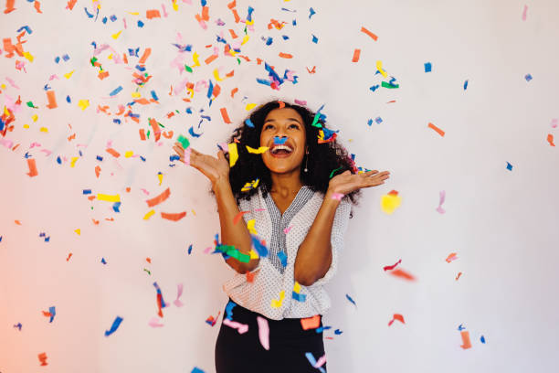 Young woman standing indoors under colorful confetti Young woman standing indoors under colorful confetti confetti photos stock pictures, royalty-free photos & images
