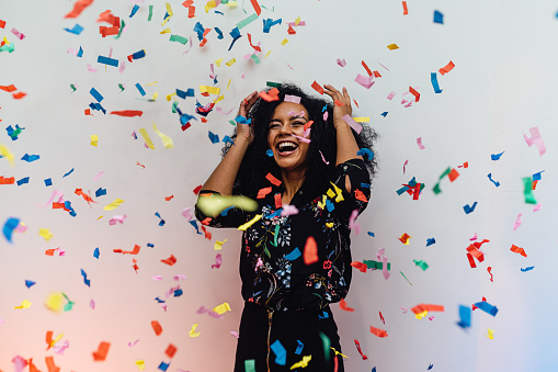 Surprised woman standing indoors while colorful confetti falling
