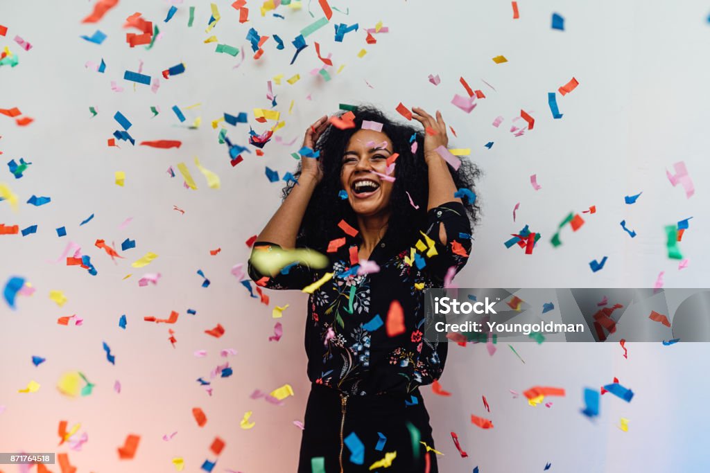 Surprised woman standing indoors while colorful confetti falling Confetti Stock Photo