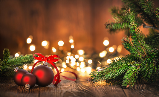 Red Christmas Ornaments on Wood Background and defocused lights. Spruce Tree branch on the left and right.