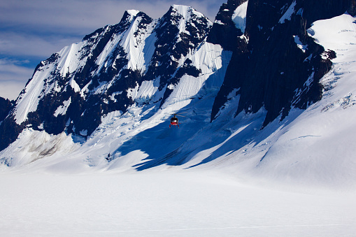 a rescue helicopter flying in the mountains is dwarfed in size by its surroundings.