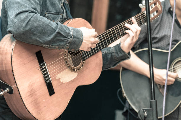 Musician playing acoustic guitar in a concert show Two males musicians playing acoustics guitars in a concert show. Close shooting of hands playing a wood made guitar, the artists are dressing by jean jacket and blue t-shirt. string ensemble stock pictures, royalty-free photos & images