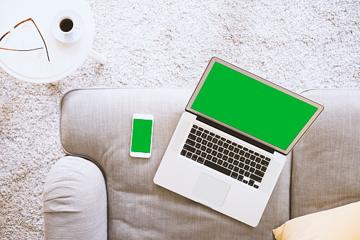 Green screen laptop and smart phone on the couch. Green screen wireless device at home.