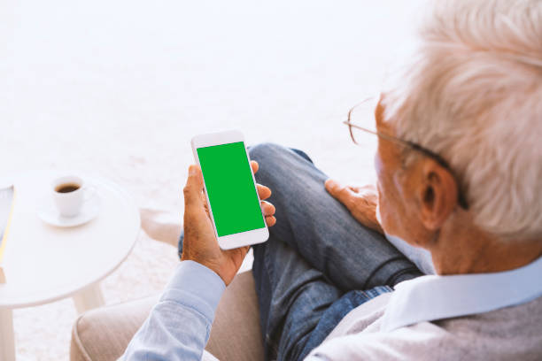 Senior man using green screen smartphone, sitting on couch Senior man sitting on couch. Using green screen smart phone at home. coffee table top stock pictures, royalty-free photos & images