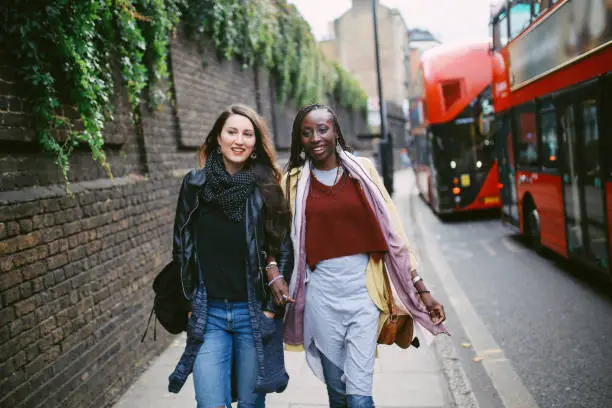 Portrait of two young women walking in Shoreditch London, spending a fun time city break on a beautiful Autumn day. They are wearing casual clothes.