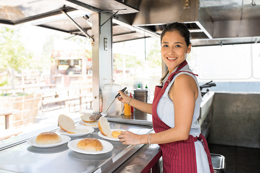 Portrait of a beautiful young food truck owner making burgers and enjoying her work