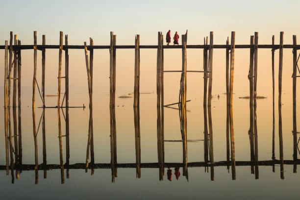 U Bein Bridge at Sunrise in Mandalay, Myanmar (Burma) Unrecognizable Buddhist monks crossing U Bein Bridge at sunrise in Mandalay, Myanmar (Burma). Amarapura stock pictures, royalty-free photos & images