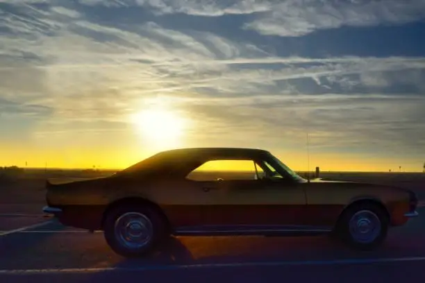 Cruiser week at Ocean City, MD draws 1000s of vintage cars of all types, here is a 70s era Camaro silhouetted against the morning sunrise in the inlet parking lot