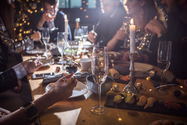 Good food brought us together Christmas dinner with friends. Home is decorated with Christmas string lights. Everyone wearing elegant clothing. Eating sushi and drinking champagne. evening meal stock pictures, royalty-free photos & images