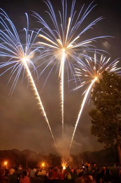 Photo of Three large colorful firework displays shoot off from the ground as a field full of spectators watch