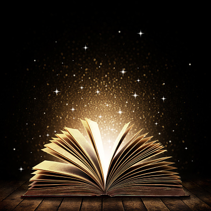 Open book on wooden vintage table with mystic magic bright light on background