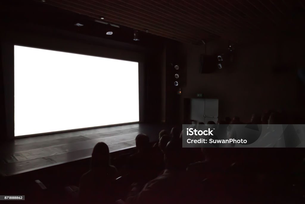 Blurry background of people watching movie in the movie theater with white screen. Movie Theater Stock Photo