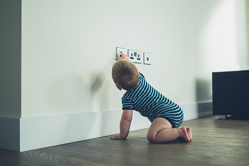 A little baby is reaching for a plug socket at home not knowing the danger