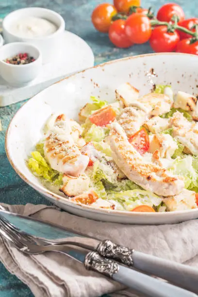 Delicious caesar salad with croutons, grilled chicken breast, grated parmesan cheese and cos lettuce, with sauce in the gravy boat, simply and healthy recipe