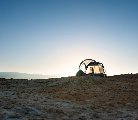 Silhouette of woman resting in translucent tent camped on wild beach in the sunset